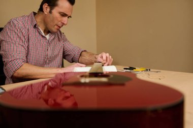 Gitar tellerini akustik gitarda dikkatlice ayarlayan ve değiştiren adam, bir ev atölyesinde enstrüman bakımını, tamirciliğini ve el işçiliğini gösteriyor..