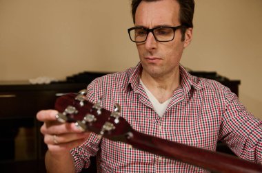 Gitar tellerini ayarlamaya ve değiştirmeye odaklanan adam, gitar bakım ve onarım tekniklerini evde göstermeye.
