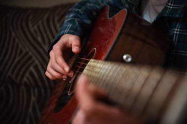 Genç çocuk evde akustik gitar tıngırdatıyor, rahat, rahat bir atmosfer yaratıyor, rahat bir oturma odasında müzik ve şarkı sözü yazıyor..