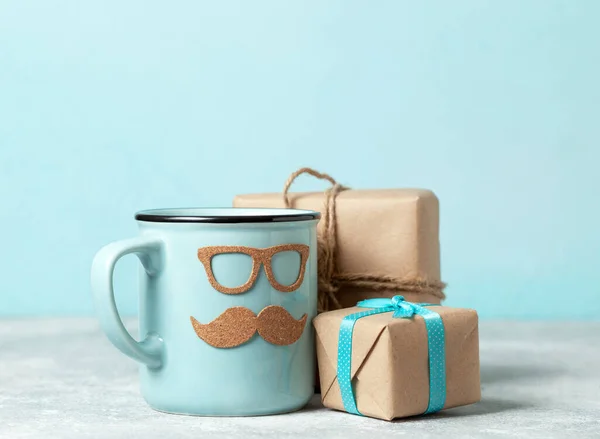 father\'s day gift concept. blue mug with mustache and glasses and gift boxes on a blue background