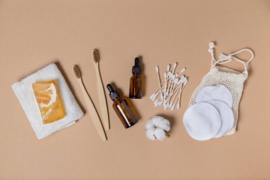 Sıfır atık, çevre dostu yaşam tarzı. Bambu diş fırçaları, bambu kulak çubukları, doğal sabun, yeniden kullanılabilir pamuk makyaj çıkarıcı mendiller, bej arka planda yeniden kullanılabilir şişeler. Yukarıdan görünüm.