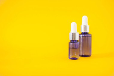 Parlak sarı arka planda serumu olan kozmetik şişeleri. Kozmetik ve güzellik kavramı.