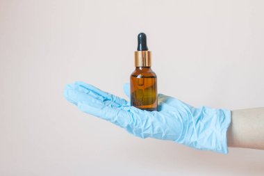 Elinde yüzü için serum olan şişeler hafif arka planda koruyucu plastik eldivenler. Güzellik endüstrisi.