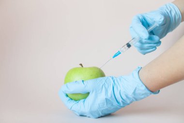Ellerinde koruyucu plastik eldivenlerde şırınga olan yeşil bir elma.