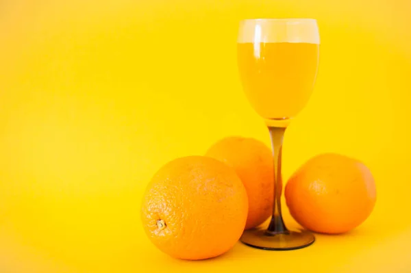 Bright oranges and a glass of orange juice on a bright yellow background. Healthy lifestyle concept. — Stock Photo, Image