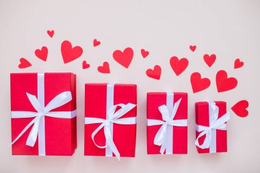 Beyaz saten kurdele ve kırmızı kalplerle bağlanmış çeşitli boylarda kırmızı hediye kutuları.