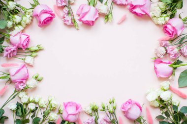 Açık pembe arka planda narin beyaz ve pembe güller ve Eustomas çerçevesi. Düzen.