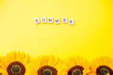 Yazın tahta bloklardan bir yazı. Parlak sarı arka planda parlak, sulu ayçiçekleri. Düzen.