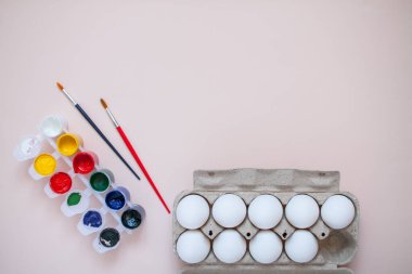 Açık pembe arka planda parlak boyalar ve iki fırça. Yumurta kaseti. Paskalya için yumurta boyamaya hazırlanıyorum..