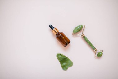 Yeşil yüz masajcısı ve açık pembe arka planda serum şişesi olan tasarım.