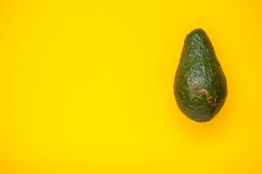 Parlak sarı bir arka planda olgun, güzel bir avokado.