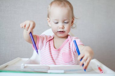 Küçük bir kız keçeli kalemlerle zevkle çizmeye çalışır.