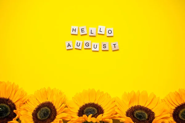Inscription from wooden blocks hello august. Bright juicy sunflowers on a bright yellow background. Layout. — Stock Photo, Image