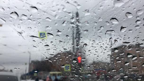 Curah hujan jatuh di atas gelas mobil. Mobil itu berdiri dan menunggu di lampu lalu lintas. — Stok Video