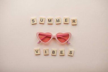 Yerleşim planı. Açık pembe arka planda kalp şeklinde pembe gözlük. Tahta blokların yazıtları Yaz titreşimleri