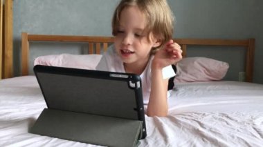 A little girl lies on the bed and communicates online. Learning online. Calling family