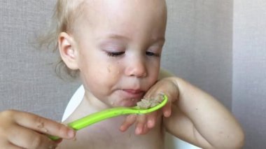 Zevkli ve ilgili küçük bir kız kendi başına yulaf lapası yemeye çalışır.