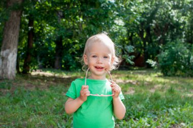 Yeşil tişörtlü ve pembe kalp şeklinde güneş gözlüklü küçük kız yazın parkta yürüyor.
