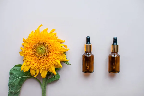 Pose plate de tournesols et de bouteilles pour sérum cosmétique ou crème sur un fond rose clair. Le concept de beauté et de préservation de la jeunesse — Photo