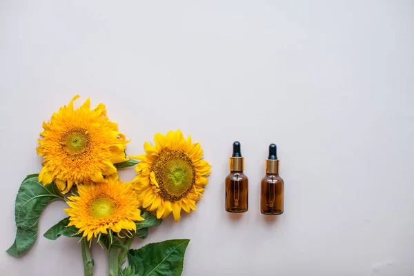 Colocación plana de girasoles y botellas para suero cosmético o crema sobre un fondo rosa claro. El concepto de belleza y preservación de la juventud —  Fotos de Stock