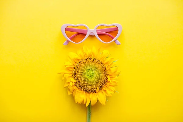 Arreglo de gafas de sol rosas en forma de corazones y girasoles sobre un fondo amarillo brillante —  Fotos de Stock