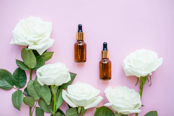 El diseño de delicadas rosas y botellas de suero cosmético sobre un fondo rosa —  Fotos de Stock