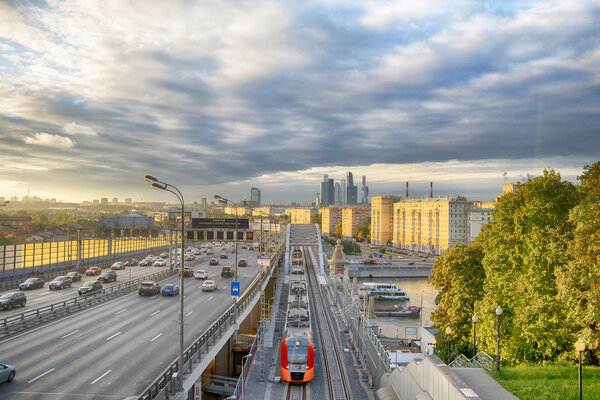 The skyscrapers, the Third Ring Road and the ES2G Lastochka (Swallow) trains on the Moscow Central Circle line at sunset. Time-lapse. Moscow. Russia