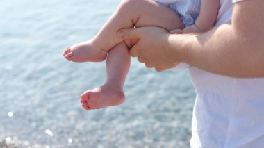 Babanın eli bebeğin ayağını tutuyor.