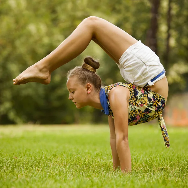 Молода дівчина розтягує вправи на зеленій траві в парку — стокове фото