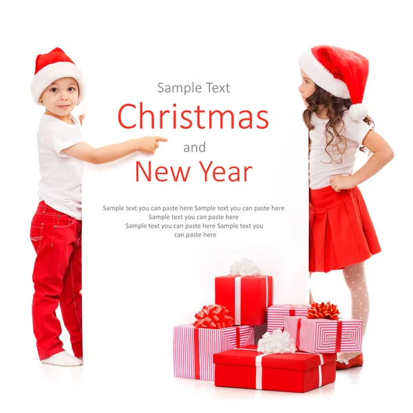 Happy little kids in Santa hat peeking from behind blank sign billboard — Stock Photo, Image