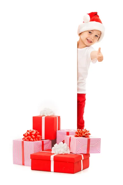 小男孩在圣诞老人的帽子后面空白标志广告牌窥视和拇指现身 — 图库照片
