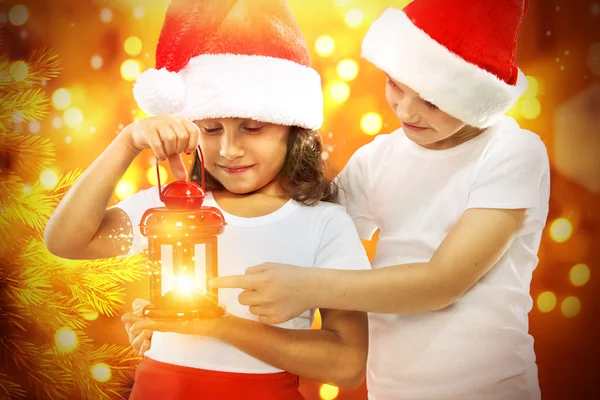 Niños felices en el sombrero de Santa mira linterna roja de Navidad —  Fotos de Stock