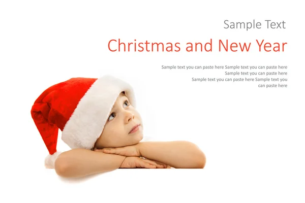 Happy little boy in Santa hat peeking from behind blank sign billboard — Stock Photo, Image