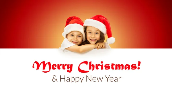 Petits enfants heureux dans le chapeau de Père Noël regardant par derrière panneau d'affichage vierge — Photo
