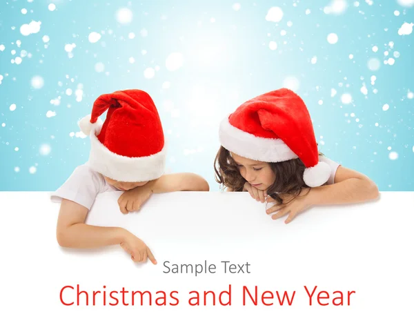 Happy little kids in Santa hat peeking from behind blank sign billboard — Stock Photo, Image