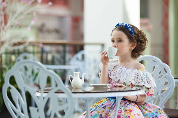 Porträt eines kleinen Mädchens in einem floralen Kleid, das Tee trinkt — Stockfoto