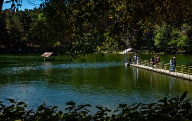 Güzel göl manzarası, mavi ve yeşil renkler, bir köprü ve insanlar.