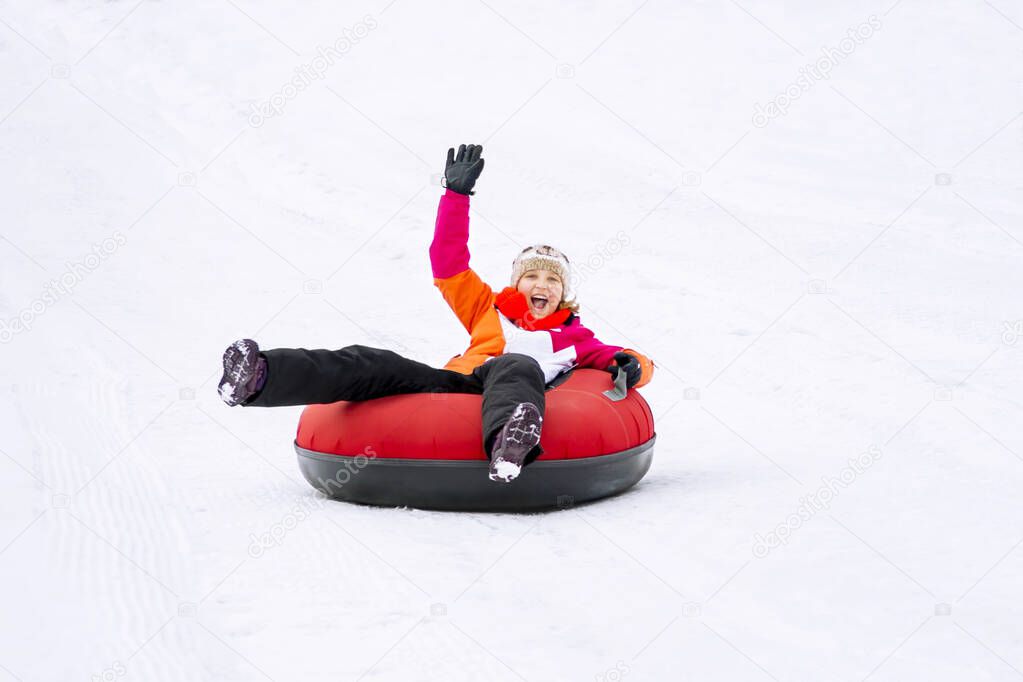 Child girl on snow tubes downhill at winter day.