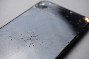 Açık gri arkaplanda, akıllı telefon ekranındaki geniş çatlakların yakın plan görüntüsü..