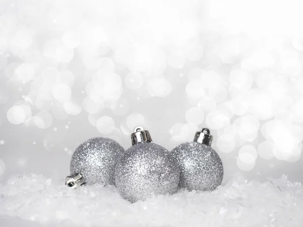 Soyut bir arka planda karda üç gümüş Noel topu..