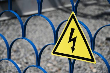 Elektrik şoku tehlikesi işareti, sarı üçgen mavi kafes üzerinde asılı..