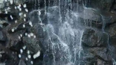 Şelaleye yakın çekim. Su büyük siyah taşların üzerinden akıyor..