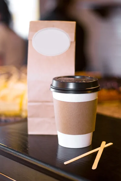 Blank paper cup of coffee and blank package in a coffee shop caf — Stock Photo, Image