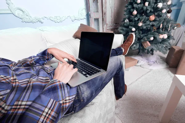 Jovem relaxante no sofá com um laptop na frente de Christm — Fotografia de Stock