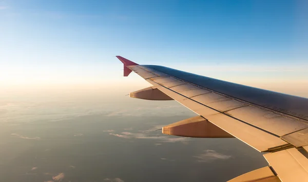 Ala de avião em voo da janela com o céu por do sol — Fotografia de Stock