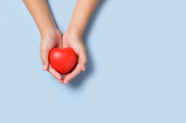 Mavi arka planda kırmızı kalbi tutan el çocuğu, bağış, mutlu gönüllü hayırseverlik, CSR sosyal sorumluluk, dünya kalp günü, dünya sağlık günü, dünya akıl sağlığı günü konsepti