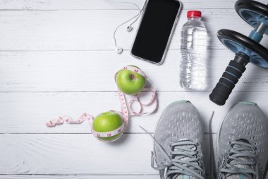 Beyaz ahşap arka planda taze su şişesinin yanında yeşil elmalı ve cep telefonlu koşu ayakkabıları, egzersiz ve diyet konsepti