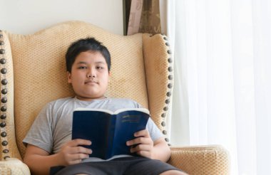 Genç çocuk evdeki sandalyede kitap okuyor. eğitim kavramı