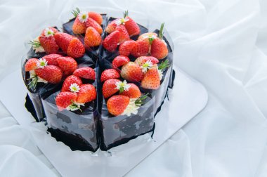 Beyaz kumaş, pasta ve fırın konseptiyle süslenmiş taze çilekle süslenmiş çikolatalı pasta.