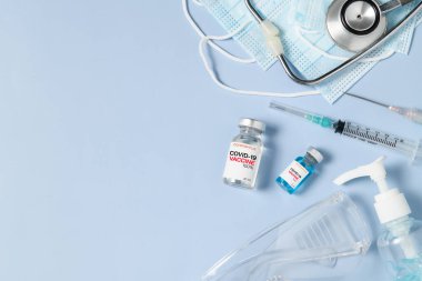 Mavi arka planda cerrahi maske, Coronavirüs veya COVID-19 salgın konseptini önlemek için şırınga ve steteskoplu Covid 19 aşısı şişesi.